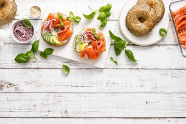 Simitli somon sandviçi, tuzlu balık, taze salatalık, beyaz arka planda soğan ve fesleğen, üst manzara. Somon tostlu sağlıklı bir kahvaltı.