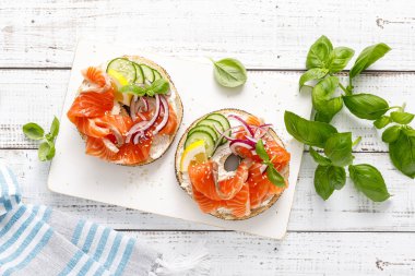 Simitli somon sandviçi, tuzlu balık, taze salatalık, beyaz arka planda soğan ve fesleğen, üst manzara. Somon tostlu sağlıklı bir kahvaltı.