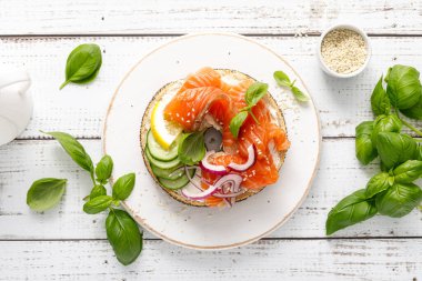 Simitli somon sandviçi, tuzlu balık, taze salatalık, beyaz arka planda soğan ve fesleğen, üst manzara. Somon tostlu sağlıklı bir kahvaltı.
