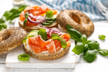 Salmon sandwiches with bagel, salted fish, fresh cucumber, onion and basil on white background. Healthy breakfast with salmon toasts