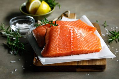 Somon balığı. Taze çiğ somon balığı filetosu. İçinde pişirme malzemeleri, otlar ve koyu arkaplanda limon var.