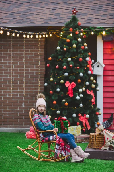 Niña Sentada Con Regalo Mecedora Fuera Casa Decorada Navidad Árbol Imágenes de stock libres de derechos