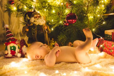 Güzel küçük bebek Noel ağacının altında yerde yatıyor Noel hediyeleri ve ışıklarla