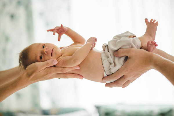 Newborn baby boy, just two weeks old, with arms of his parents holding him