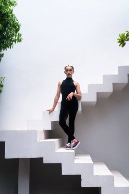 Güzel bir Asyalı eşcinsel LGBT topluluğunun vücut portresi. Bıyıklı, rujlu ve tulumlu bir adam. Modern mimari basamaklara güven yayıyor...