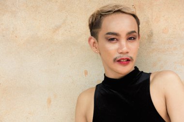 Güzel Asyalı tuhaf LGBT topluluk destekçisi ruj sürmüş ve bej duvar arkasına eşofman giymiş adam portresi
