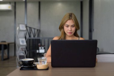 Güzel Asyalı bir kadının portresi kafede oturmuş dizüstü bilgisayar kullanırken profesyonel kıyafetler giyiyor. Giysiler iş kadını mesleğini ya da internetten öğrenim gördüğünü gösteriyor.