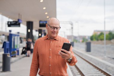 Tren istasyonunda cep telefonu kullanan yaşlı Finli adam.