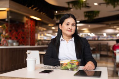 Restoranda öğle yemeğinde salata yiyen iş elbiseli kadın portresi.