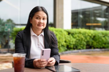 Restoranda oturmuş buzlu kahve içen Asyalı bir kadın.