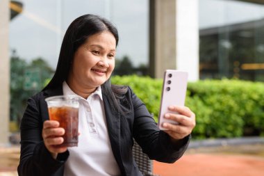 Restoranda oturmuş buzlu kahve içen Asyalı bir kadın.