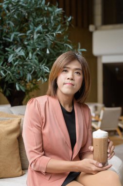 Kendine güvenen Asyalı transseksüel. İkili olmayan kişi şık bir kapalı kafe restoranında iş kıyafeti giyiyor.