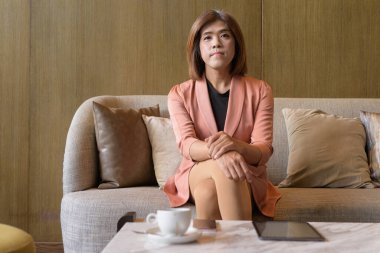 Kendine güvenen Asyalı transseksüel. İkili olmayan kişi şık bir kapalı kafe restoranında iş kıyafeti giyiyor.