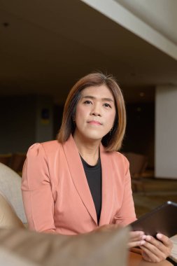 Kendine güvenen Asyalı transseksüel. İkili olmayan kişi şık bir kapalı kafe restoranında iş kıyafeti giyiyor.