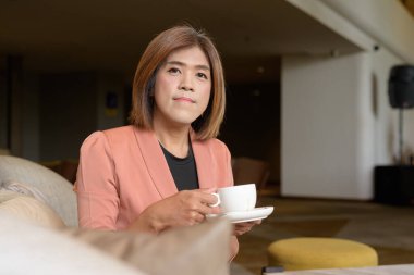 Kendine güvenen Asyalı transseksüel. İkili olmayan kişi şık bir kapalı kafe restoranında iş kıyafeti giyiyor.