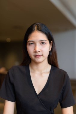 Genç Asyalı kadın kahve dükkanında oturuyor, şık siyah elbiseler giyiyor.