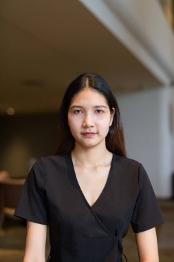 Genç Asyalı kadın kahve dükkanında oturuyor, şık siyah elbiseler giyiyor.