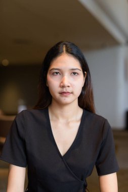 Genç Asyalı kadın kahve dükkanında oturuyor, şık siyah elbiseler giyiyor.