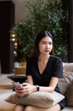 Genç Asyalı kadın kahve dükkanında oturuyor, şık siyah elbiseler giyiyor.