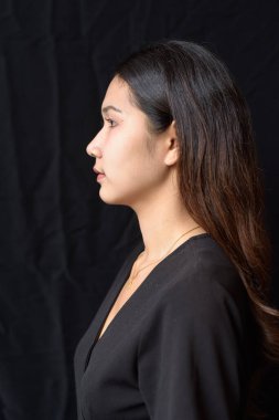 Siyah elbiseli genç Asyalı kadın siyah perdeye karşı doğal ışıkta poz veriyor.