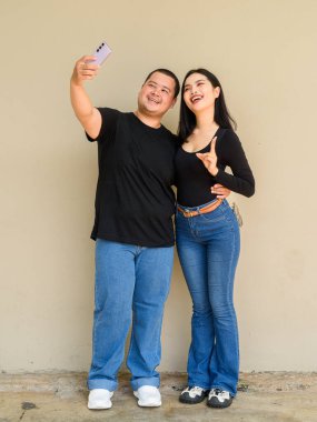 Genç Asyalı bir çiftin duvar arkasının tam boy portresi.