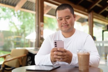 Kafe restoranında oturan Asyalı genç ve cüsseli mutlu adam.