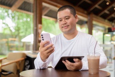 Kafe restoranında oturan Asyalı genç ve cüsseli mutlu adam.