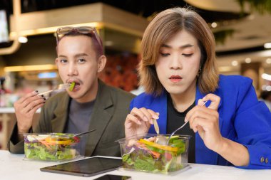 Cinsiyet farklılığı olan Asyalı iş arkadaşları salata yiyor ve dijital olarak çalışıyorlar.