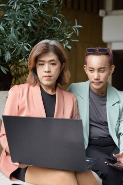 Asyalı transseksüel kadın ve kafede uzaktan çalışan ikili olmayan iş arkadaşları.