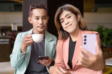 Asyalı transseksüel kadın ve kafede uzaktan çalışan ikili olmayan iş arkadaşları.