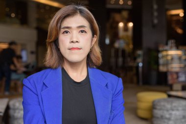 Takım elbiseli, kendine güvenen Asyalı transseksüel kadın kahve dükkanında tek başına oturuyor.