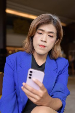 Takım elbiseli, kendine güvenen Asyalı transseksüel kadın kahve dükkanında tek başına oturuyor.