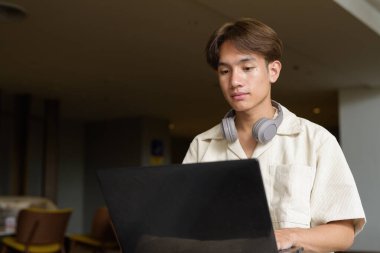 Modern kahve dükkanında oturan Asyalı yakışıklı olmayan çift yönlü öğrenci.