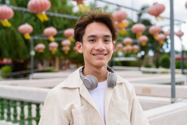 Kulaklıklı Asyalı genç turist göl kenarındaki parkta dinleniyor.