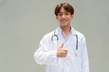 Genç Asyalı sağlık çalışanı laboratuvar önlüğü giyiyor.