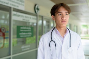 Genç Asyalı sağlık çalışanı kliniğin önünde laboratuvar önlüğü giyiyor.