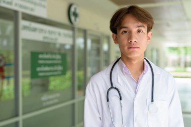 Genç Asyalı sağlık çalışanı kliniğin önünde laboratuvar önlüğü giyiyor.