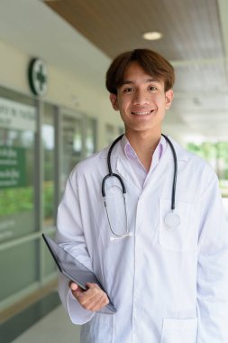 Genç Asyalı sağlık çalışanı kliniğin önünde laboratuvar önlüğü giyiyor.