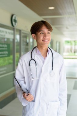 Genç Asyalı sağlık çalışanı kliniğin önünde laboratuvar önlüğü giyiyor.