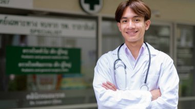 Genç Asyalı sağlık çalışanı kliniğin önünde laboratuvar önlüğü giyiyor.