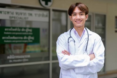 Genç Asyalı sağlık çalışanı kliniğin önünde laboratuvar önlüğü giyiyor.