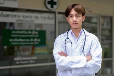 Genç Asyalı sağlık çalışanı kliniğin önünde laboratuvar önlüğü giyiyor.