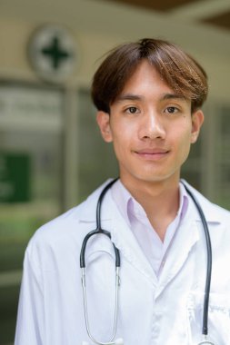 Genç Asyalı sağlık çalışanı kliniğin önünde laboratuvar önlüğü giyiyor.