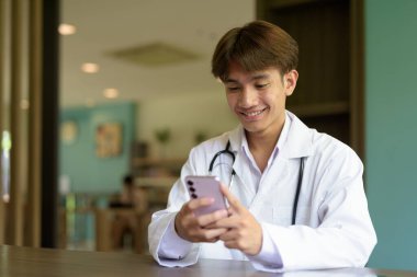 Genç Asyalı sağlık görevlisi laboratuvar önlüğü giyip içeride oturuyor.