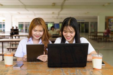 İki Taylandlı kız öğrenci açık havada bir üniversite kafesinde oturuyor. Arkadaşlık ya da çift sahnesi, gündelik yaşam tarzı, eğitim ve gençlik kültürü.