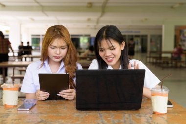 İki Taylandlı kız öğrenci açık havada bir üniversite kafesinde oturuyor. Arkadaşlık ya da çift sahnesi, gündelik yaşam tarzı, eğitim ve gençlik kültürü.