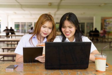 İki Taylandlı kız öğrenci açık havada bir üniversite kafesinde oturuyor. Arkadaşlık ya da çift sahnesi, gündelik yaşam tarzı, eğitim ve gençlik kültürü.