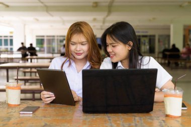 İki Taylandlı kız öğrenci açık havada bir üniversite kafesinde oturuyor. Arkadaşlık ya da çift sahnesi, gündelik yaşam tarzı, eğitim ve gençlik kültürü.