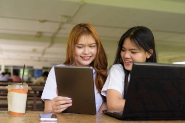 İki Taylandlı kız öğrenci açık havada bir üniversite kafesinde oturuyor. Arkadaşlık ya da çift sahnesi, gündelik yaşam tarzı, eğitim ve gençlik kültürü.