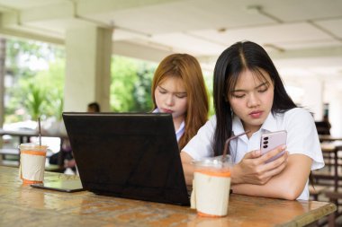 İki Taylandlı kız öğrenci açık havada bir üniversite kafesinde oturuyor. Arkadaşlık ya da çift sahnesi, gündelik yaşam tarzı, eğitim ve gençlik kültürü.